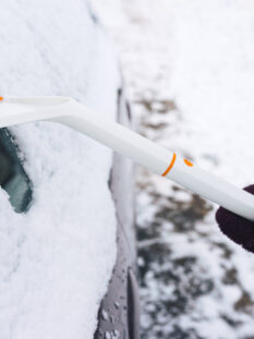 Woman cleans snow from a car with a scraper and a brush